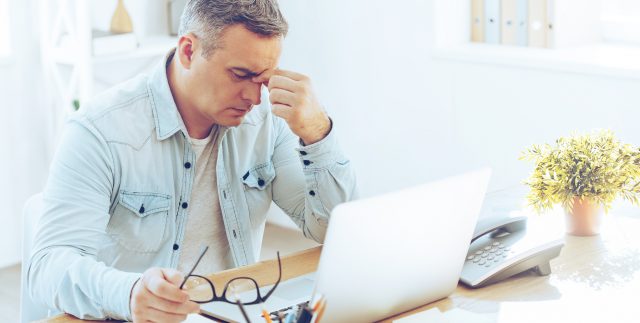 A dehydrated man pinches between his eyes while sitting at a desk and looking at a computer screen in Houston, TX