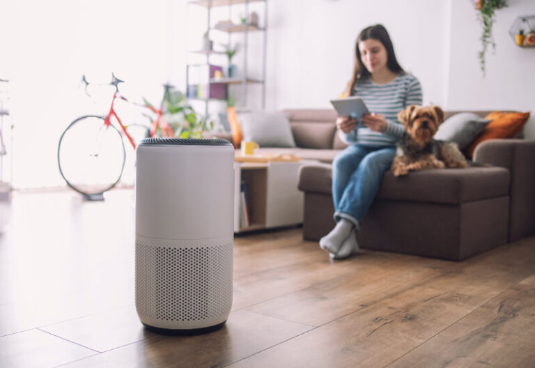 A girl sits with her dog and a tablet controlling an air purifier in the foreground