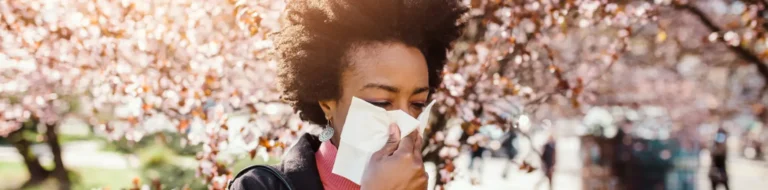 A woman blows her nose walking near blooming cherry trees in Houston, TX.