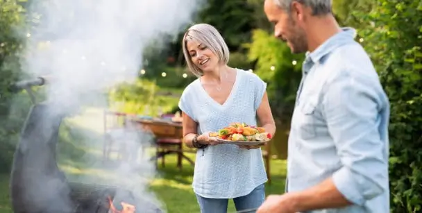 A couple stands near a grill holding hot food